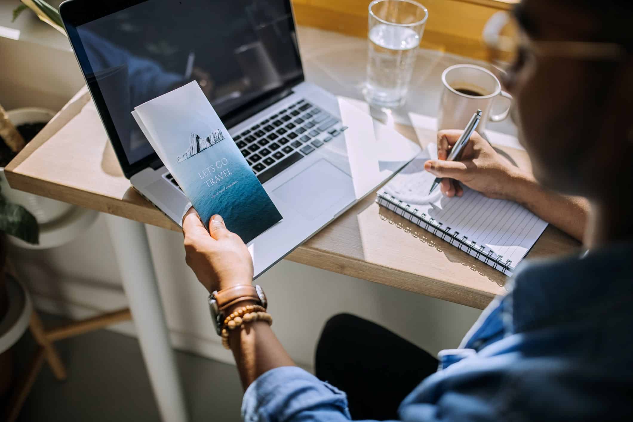 man at computer looking at travel brochure